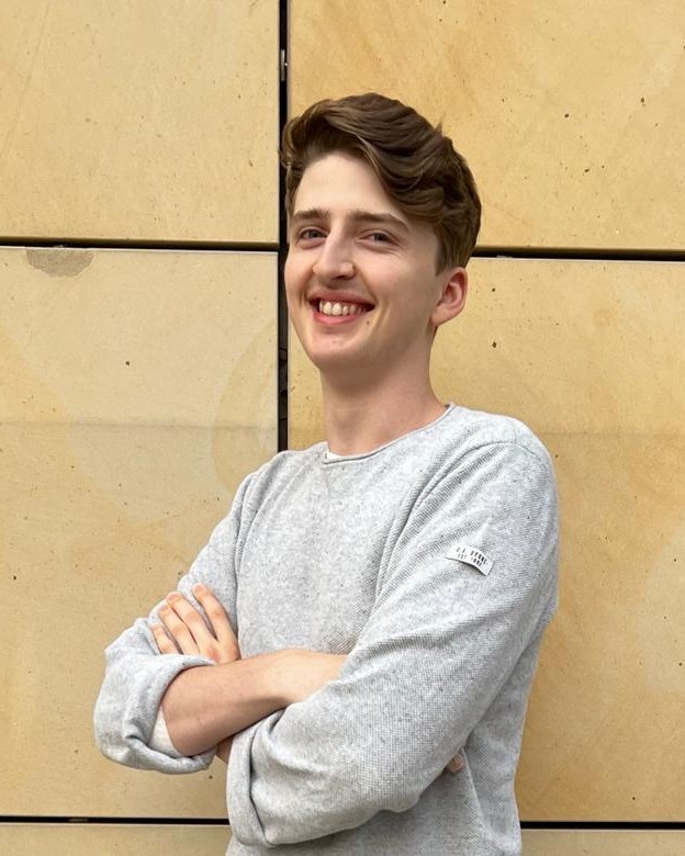 Chris-Alexander Pyschneu, lächelnd mit verschränkten Armen vor einer Sandsteinwand